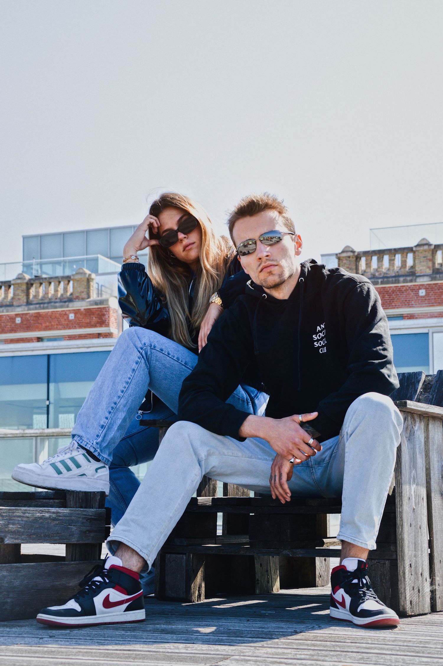 Casual couple relaxing on wooden deck wearing jeans and sneakers.