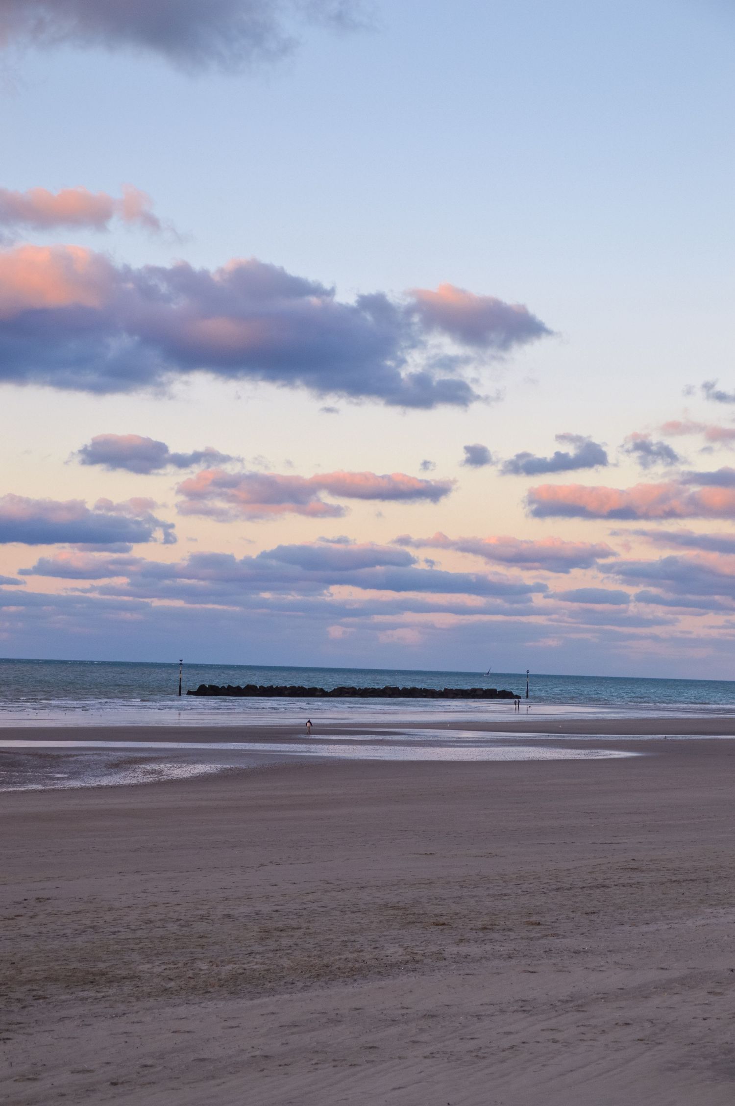 Serene beach landscape with pastel sunset clouds over calm ocean waters.