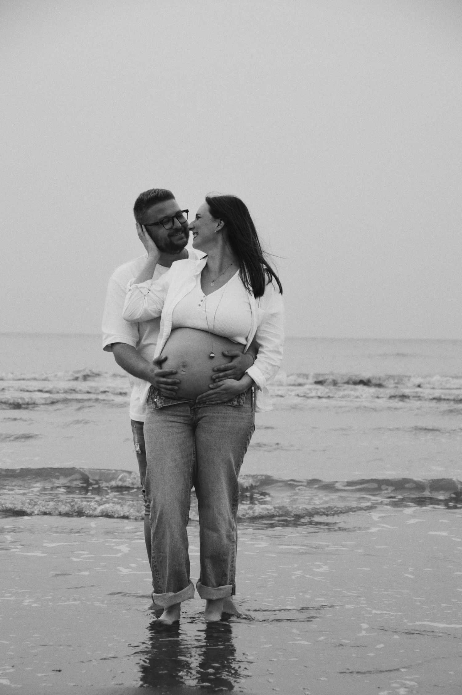 A couple wades in shallow ocean water during their black and white beach photoshoot.