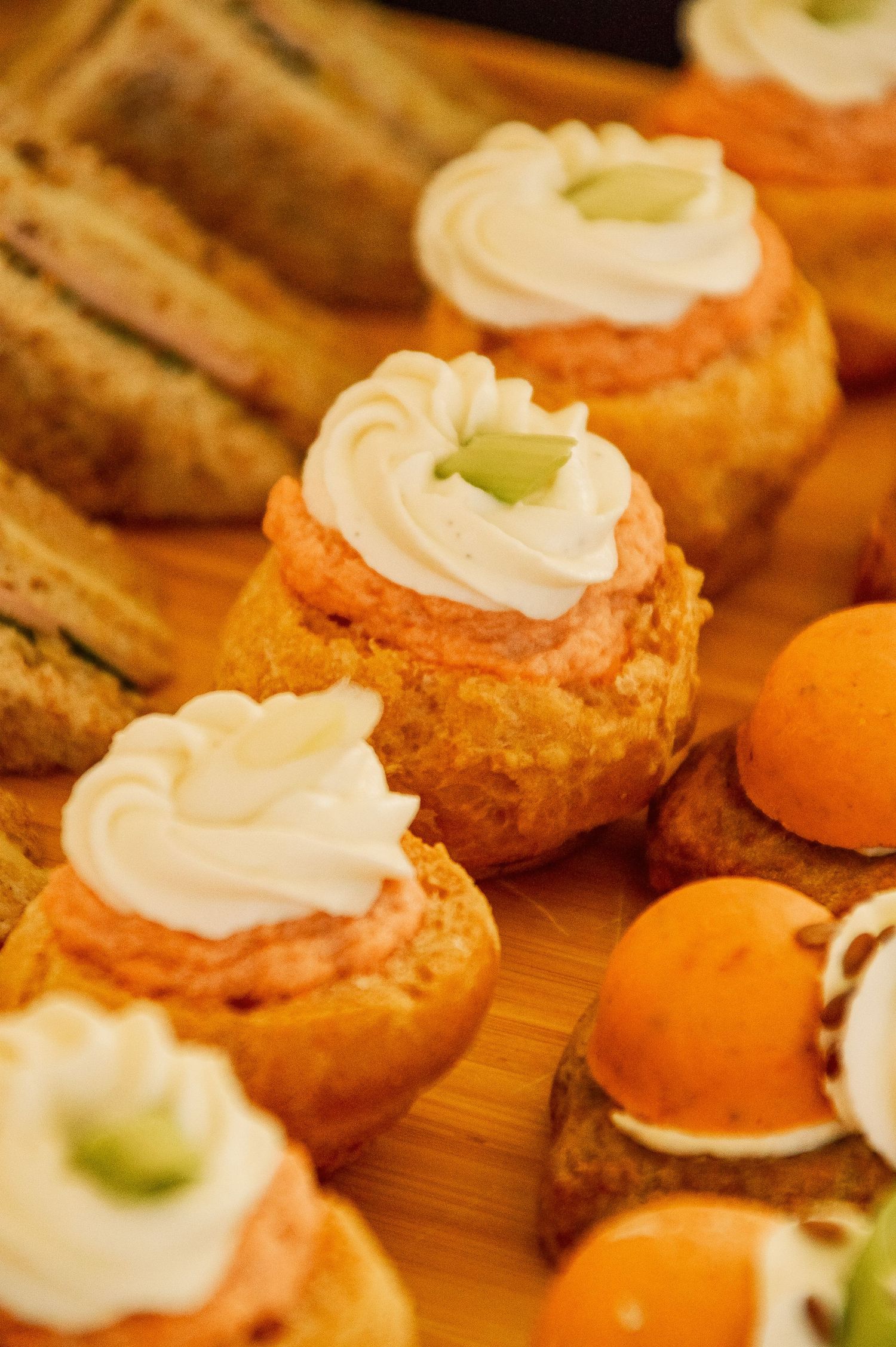 Cream-topped pastry puffs garnished with green herbs arranged on wooden surface.