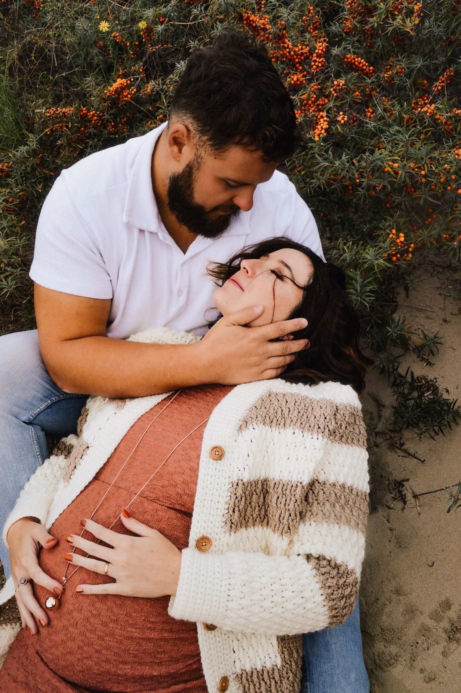 Romantic couple cuddling with cozy blanket against orange berry bushes.