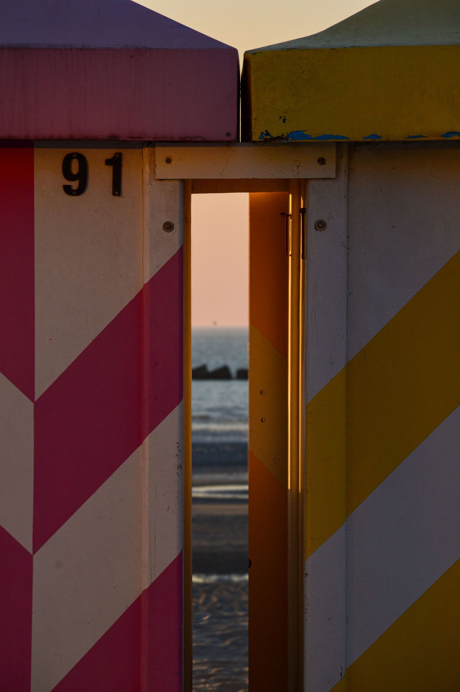 Colorful beach cabins with diagonal stripes stand in a row at sunset.