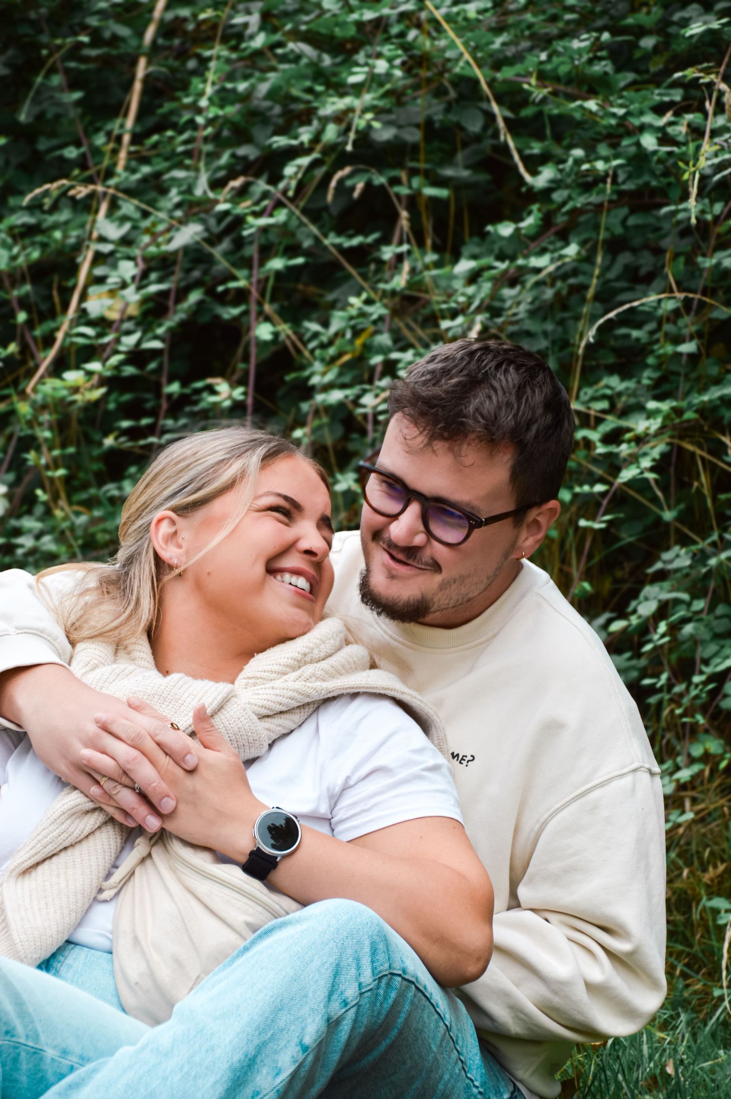 Two people embracing and laughing while sitting in a natural outdoor setting.