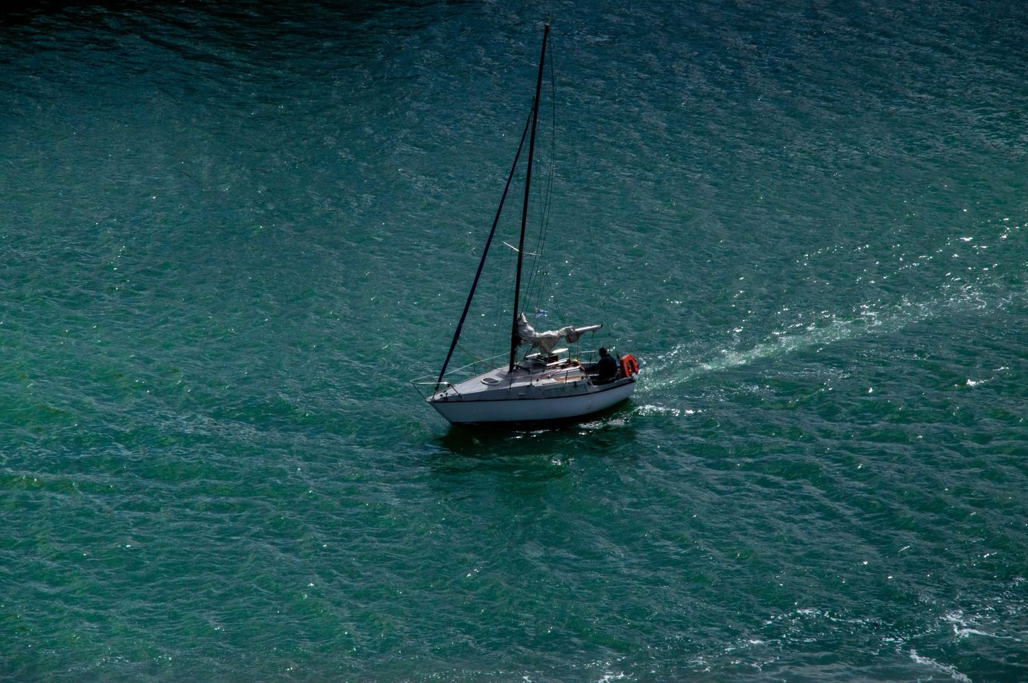 A small white sailboat navigating turquoise waters, leaving a gentle wake behind it.