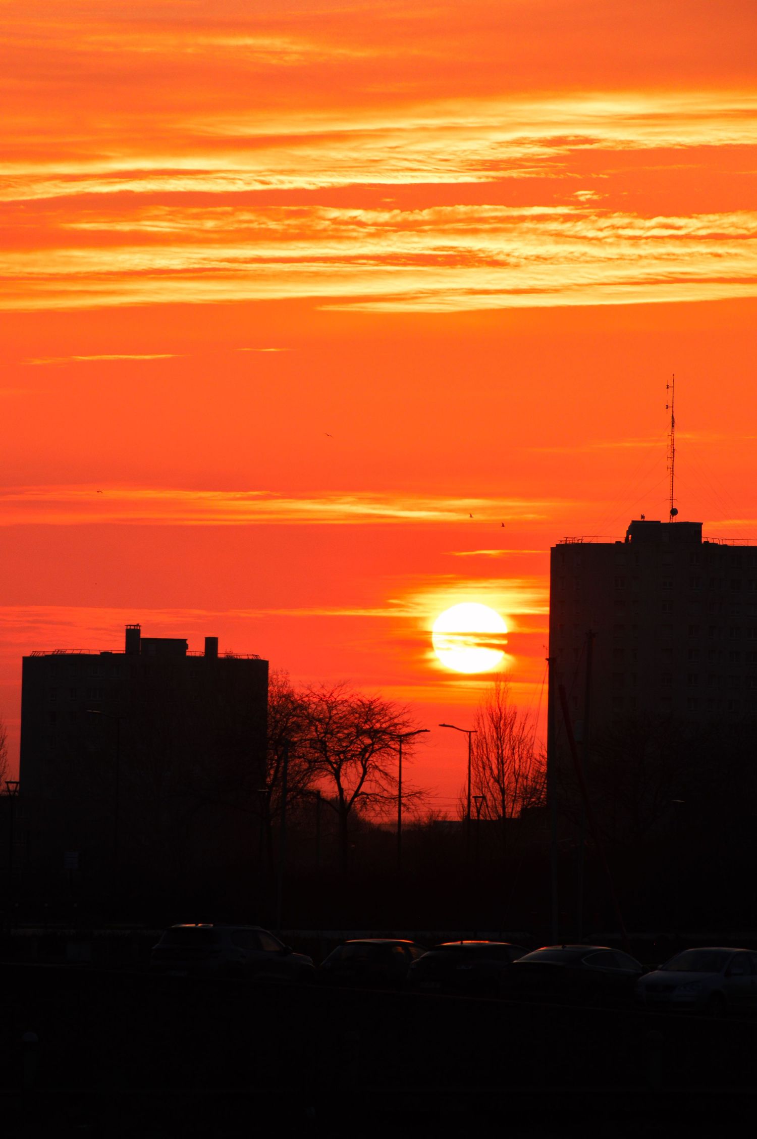 Bâtiments de la ville de Dunkerque en silhouette sur un ciel de coucher de soleil orange éclatant, avec des nuages en couches.