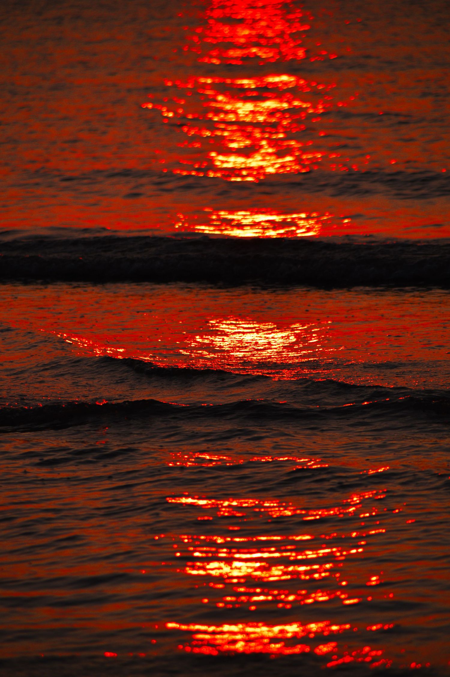 Red sunset reflection creates dramatic patterns on dark ocean waves.