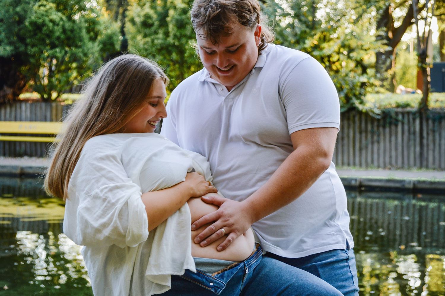 Couple in white shirts sharing intimate moments by a pond in a park setting.