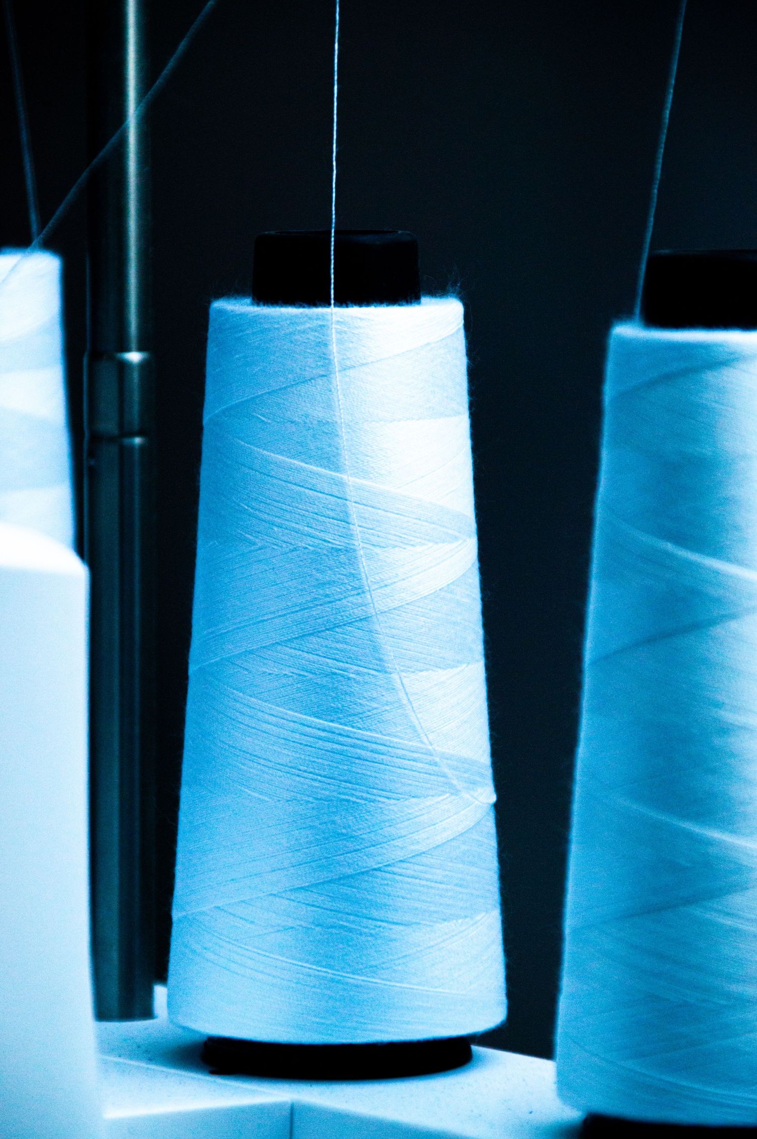 Close-up of large blue thread spools on an industrial sewing machine, illuminated with cool blue lighting.