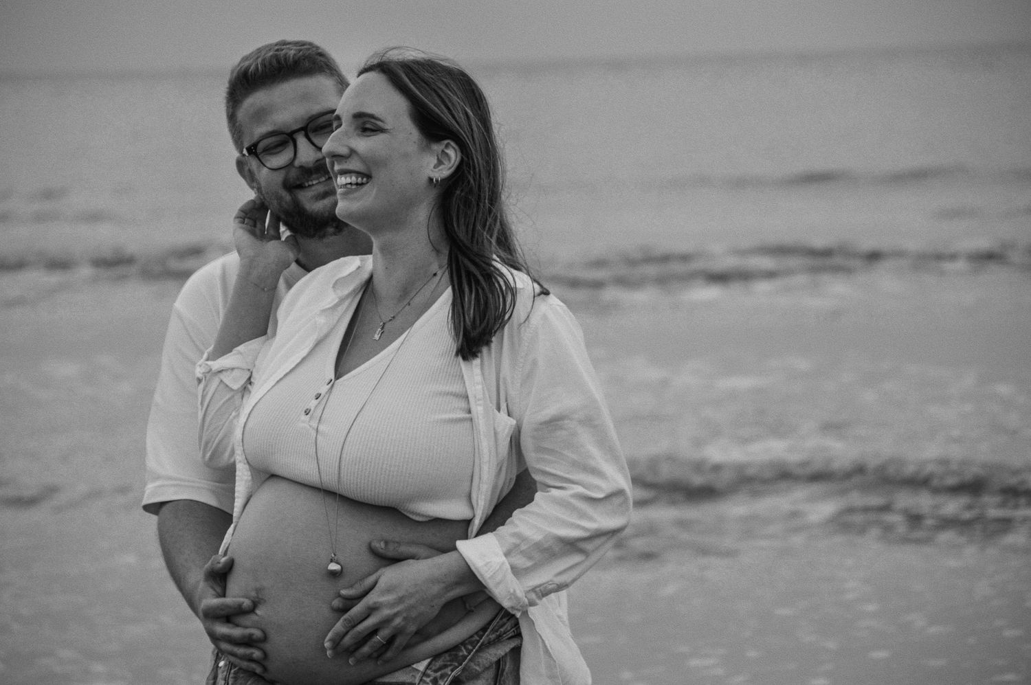 Maternity photoshoot at the beach featuring a white button-down shirt and jeans.