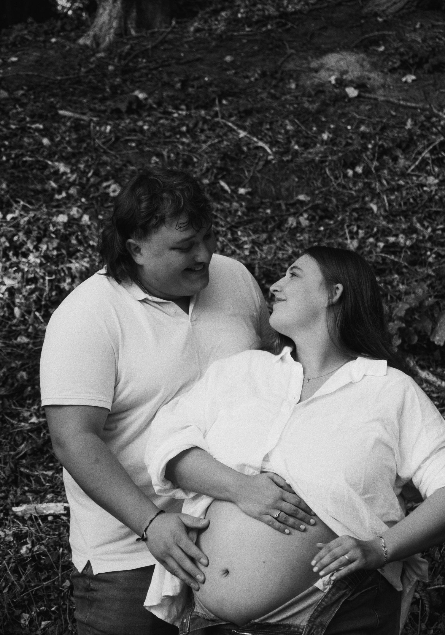 Black and white maternity photos showing intimate moments between expecting couple on dark background.