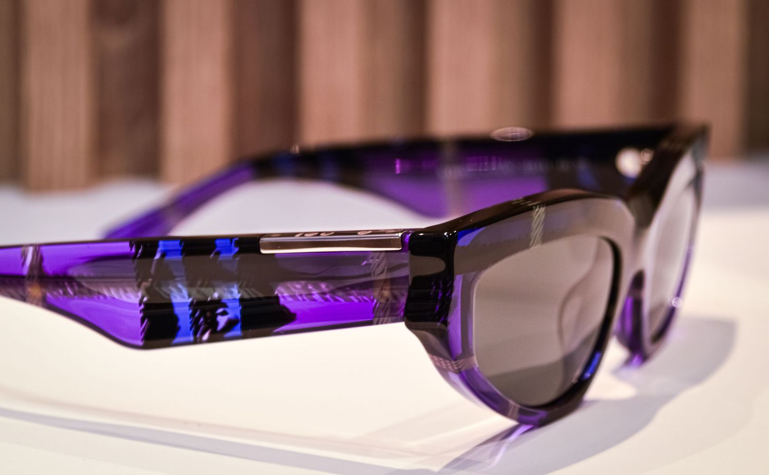 Designer sunglasses displayed on white surface with purple lighting accent.
