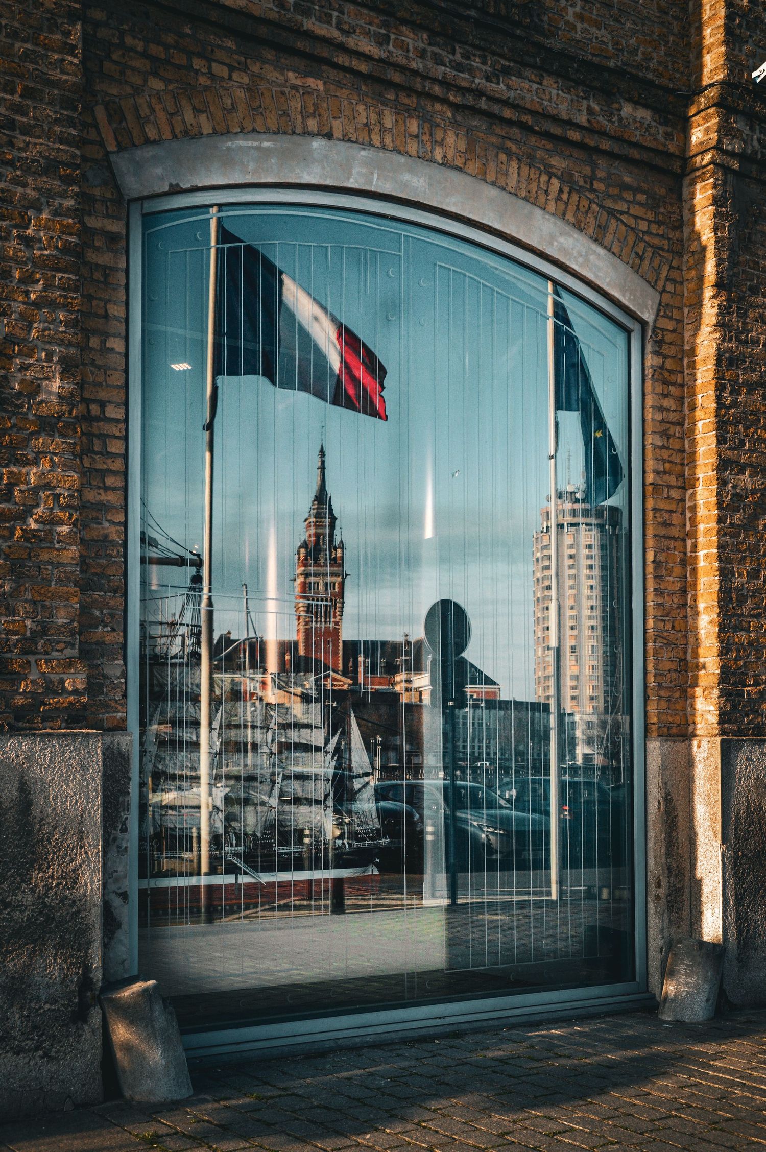 Modern cityscape reflected in arched windows of historic brick building.