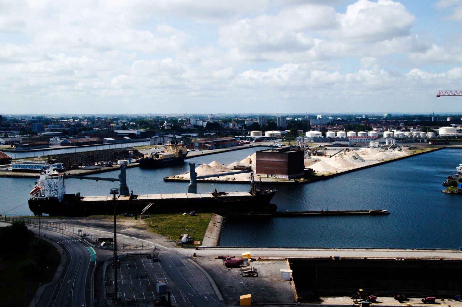Aerial view of a busy industrial port with large cargo ships docked along the waterway, surrounded by storage facilities.