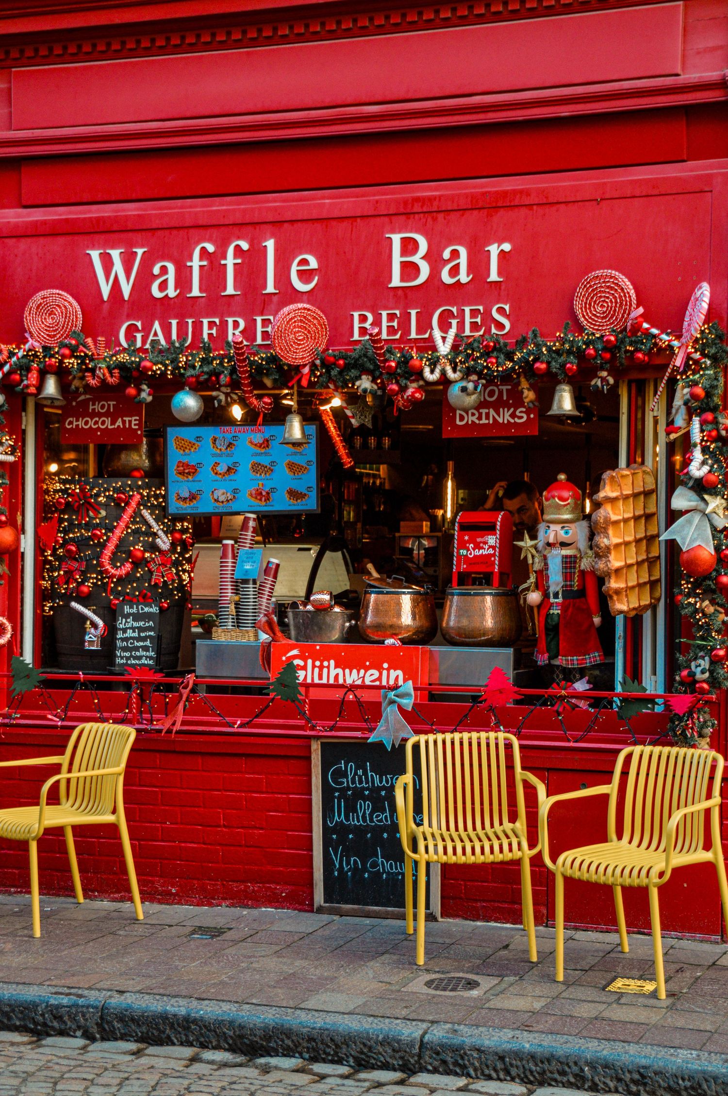 Festive red Waffle Bar storefront with yellow chairs and Christmas decorations.