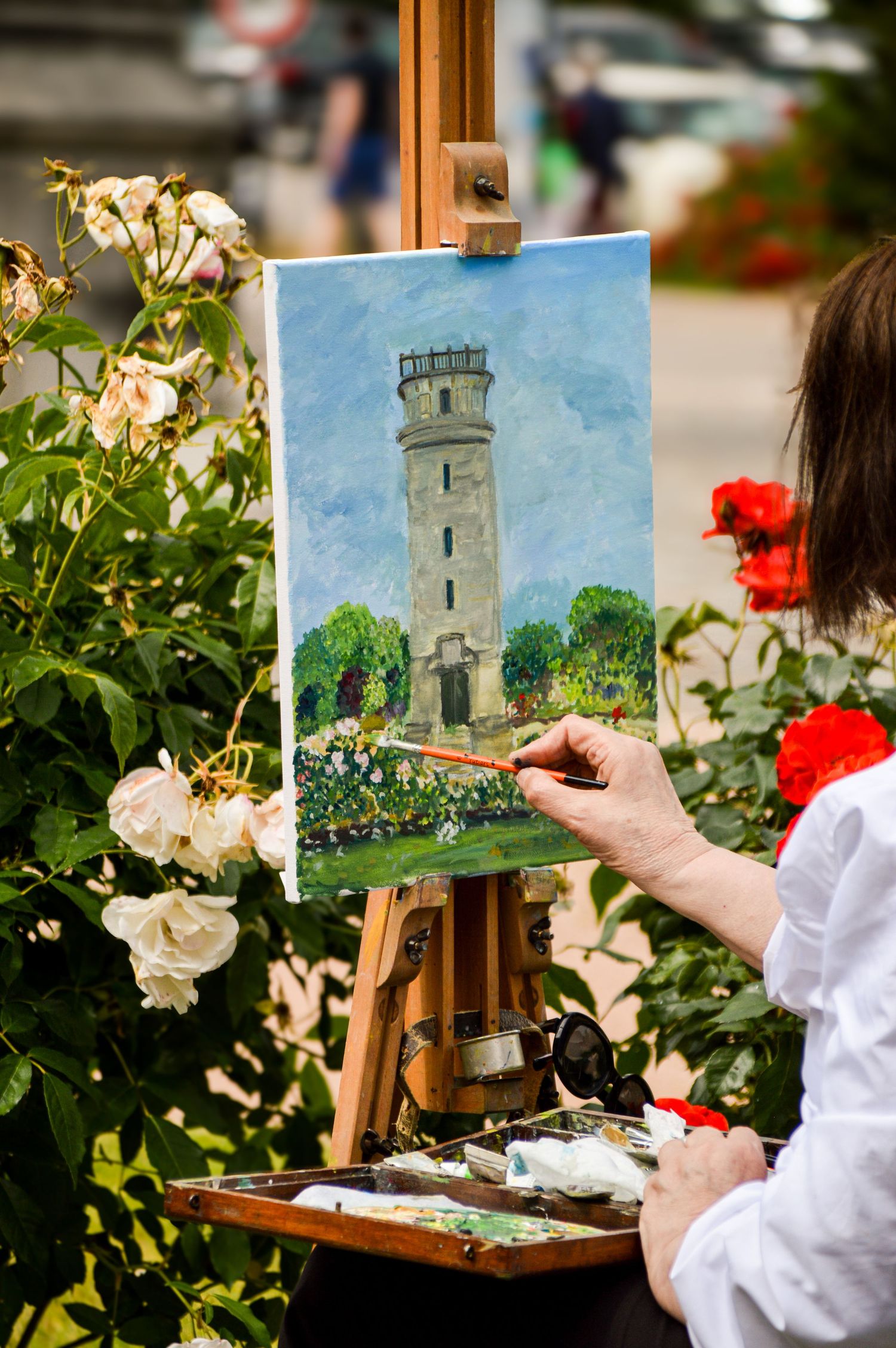Artist painting a castle tower on canvas surrounded by blooming white roses.