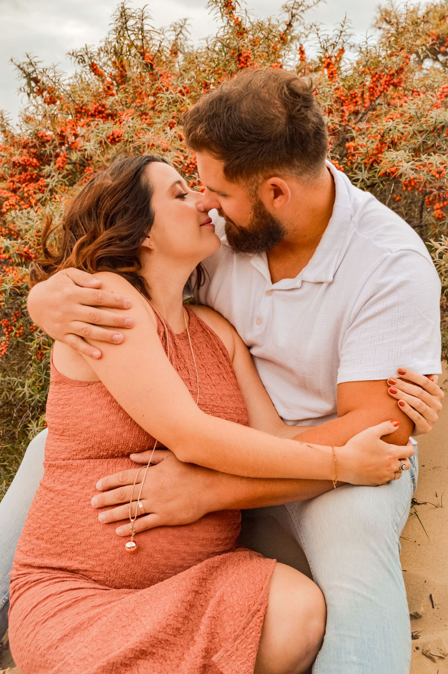 Intimate maternity photoshoot in front of red berries and autumn foliage.