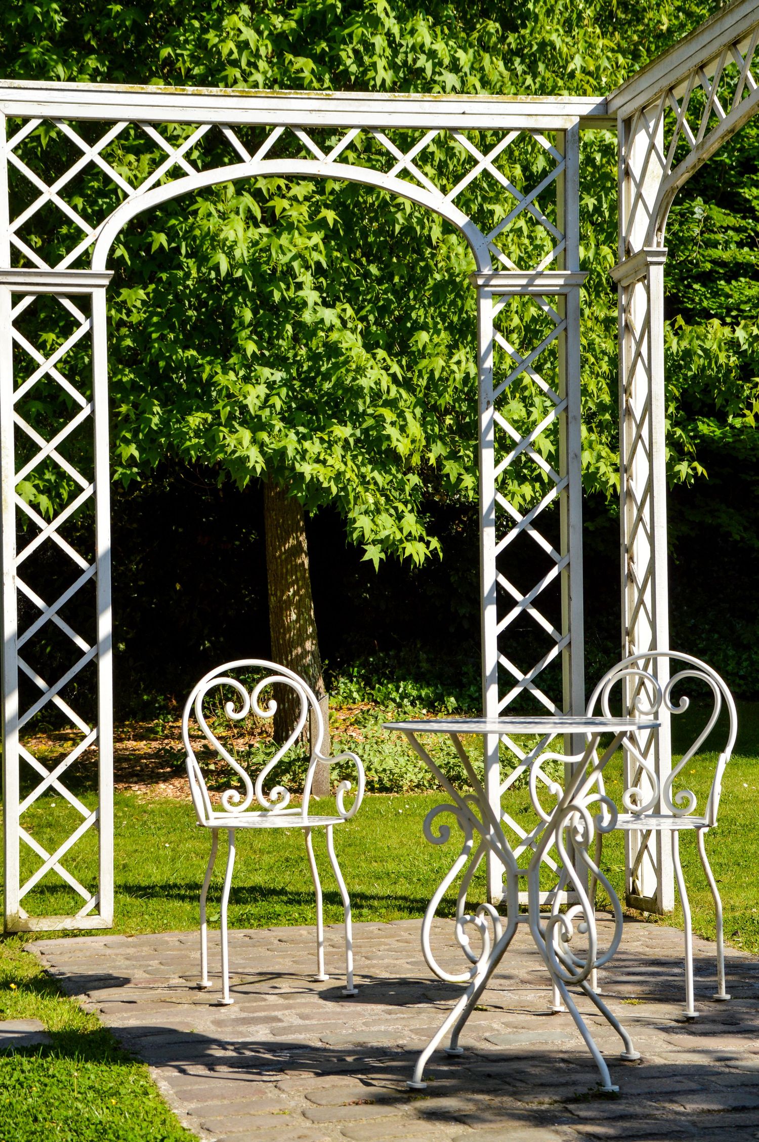 White lattice pergola with decorative metal chairs creates an inviting outdoor seating area.