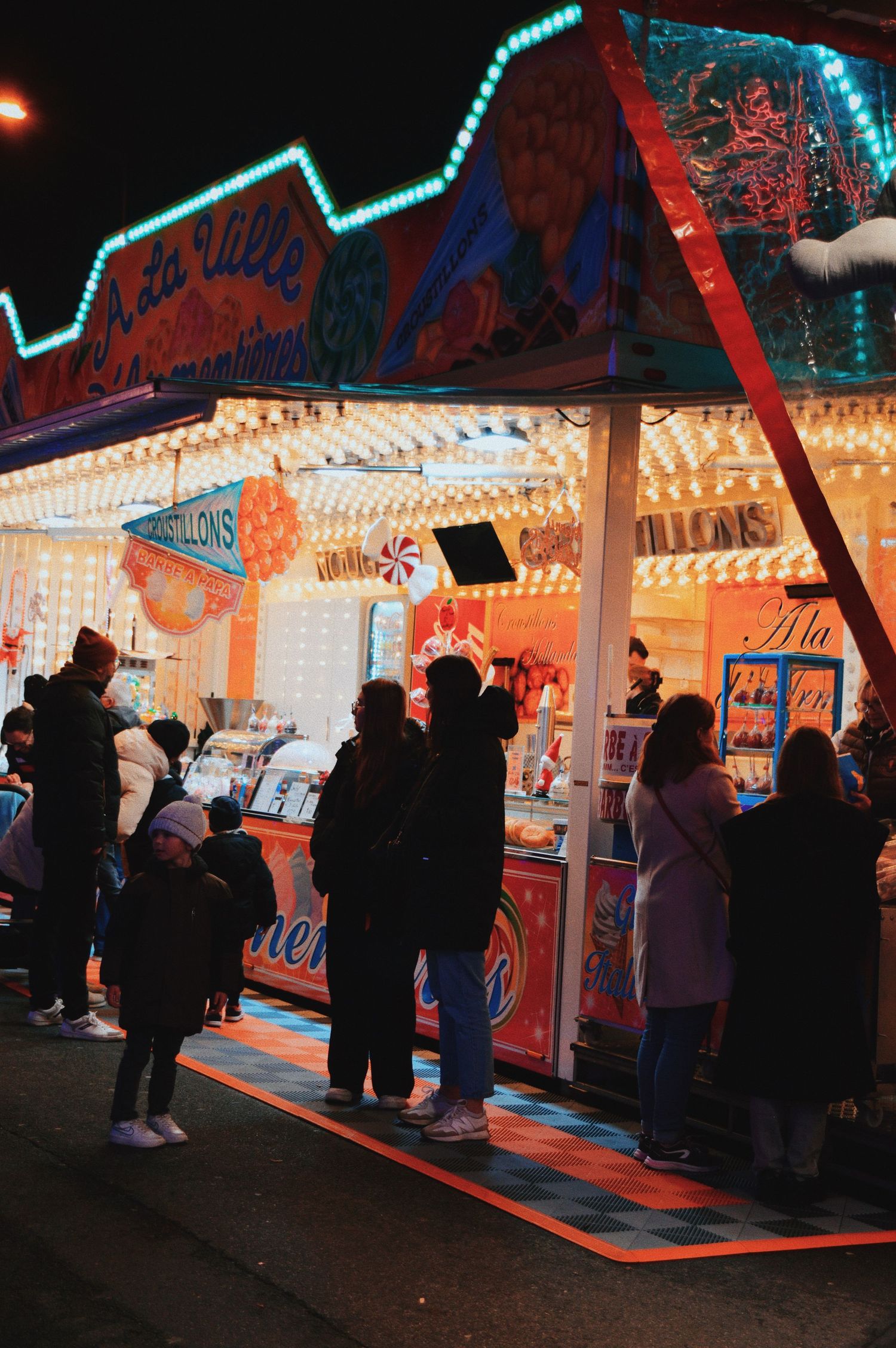Carnival game booths lit up at night with colorful neon lights and waiting customers.