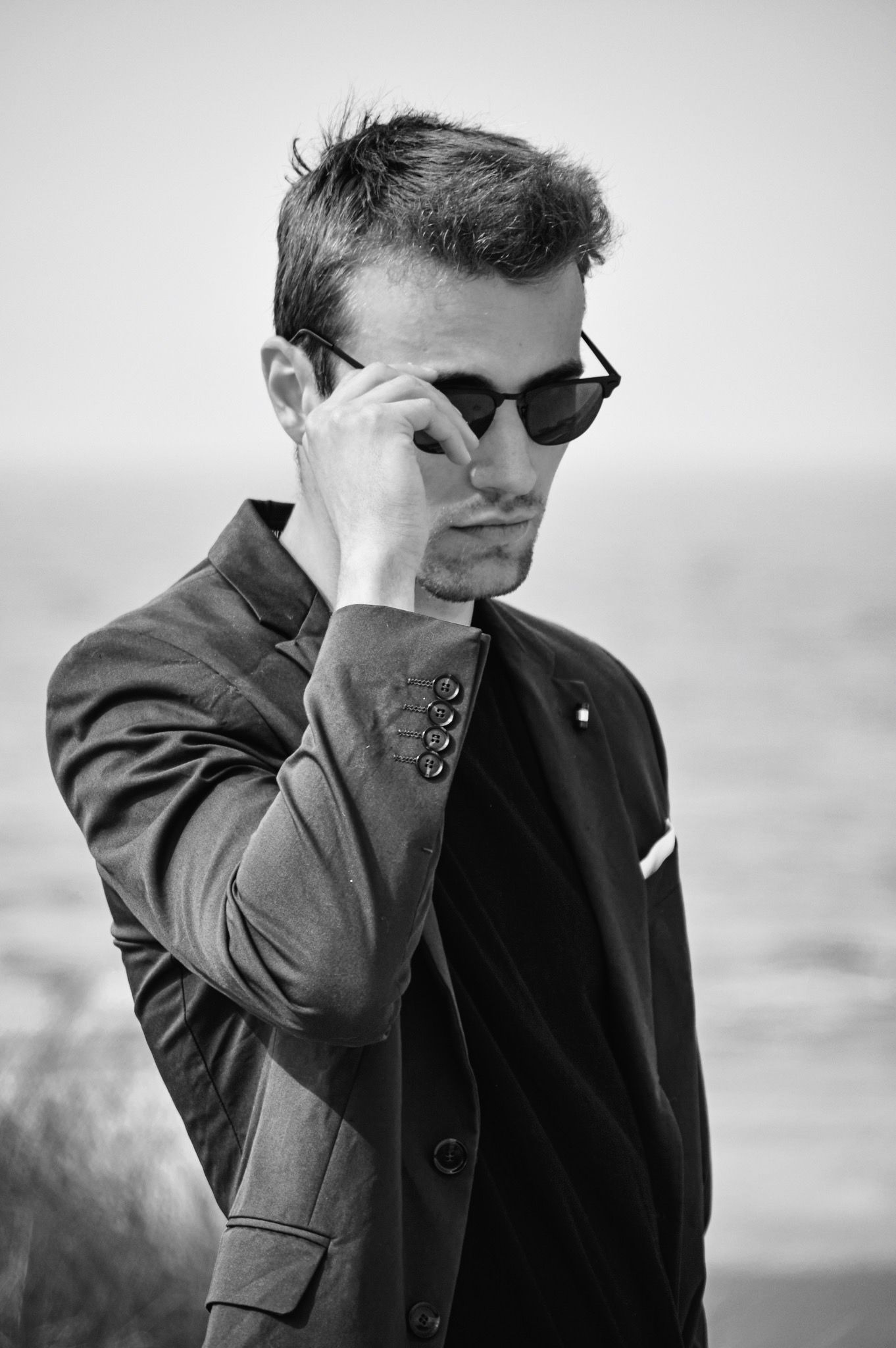 Black and white portrait of person in sunglasses and suit jacket.
