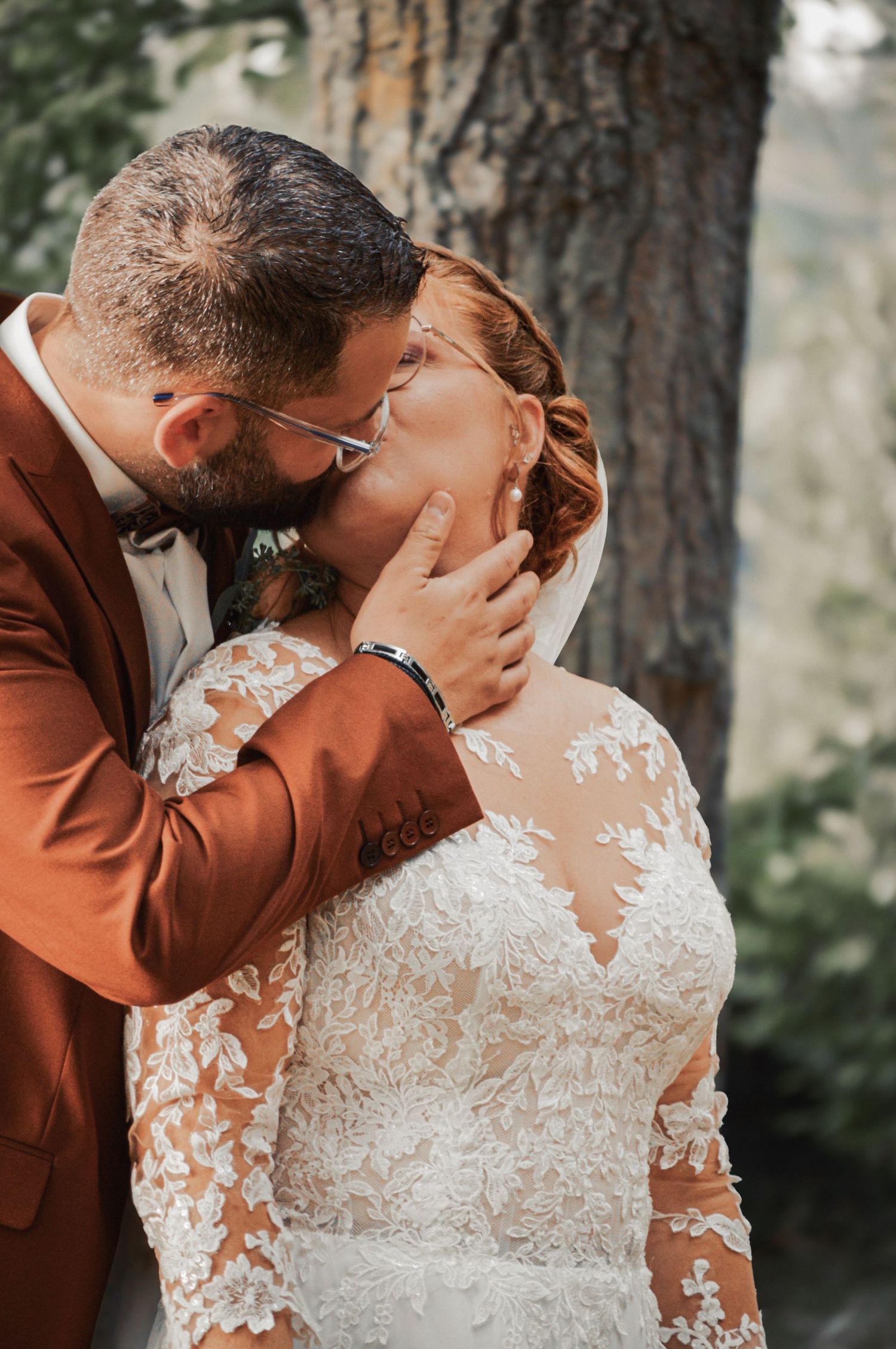 Wedding couple in rust-colored suit and lace dress sharing intimate moments outdoors.