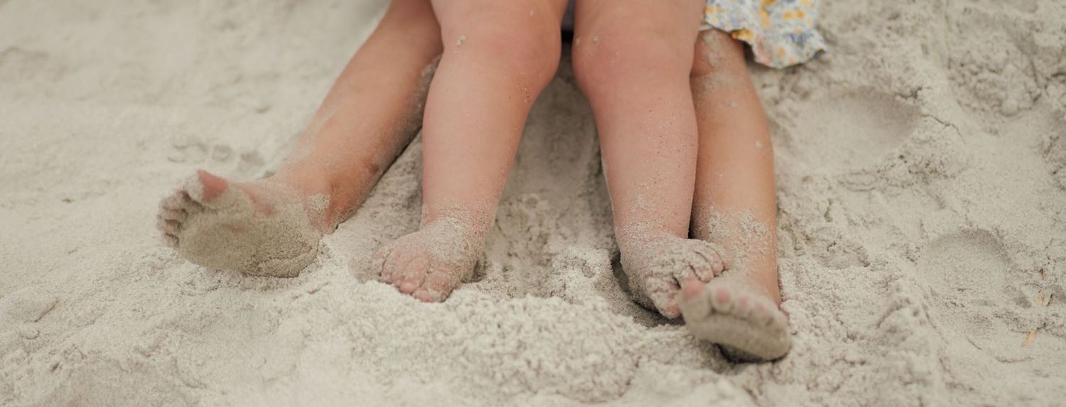 Two children's sandy feet resting on a beach, enjoying a sunny day by the shore.