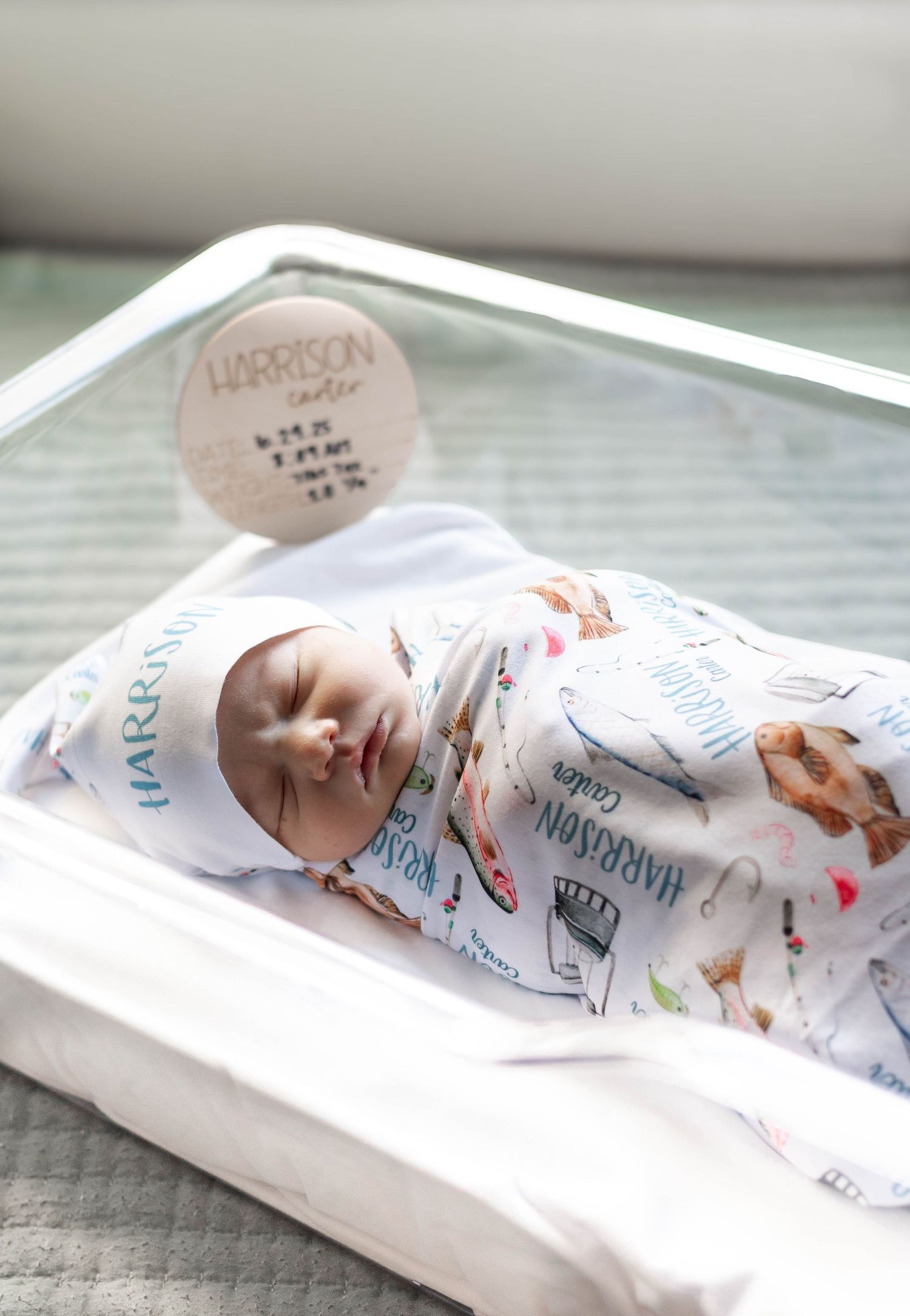 Newborn baby Harrison Carter swaddled in personalized blanket sleeping peacefully in hospital bassinet with birth stats sign.
