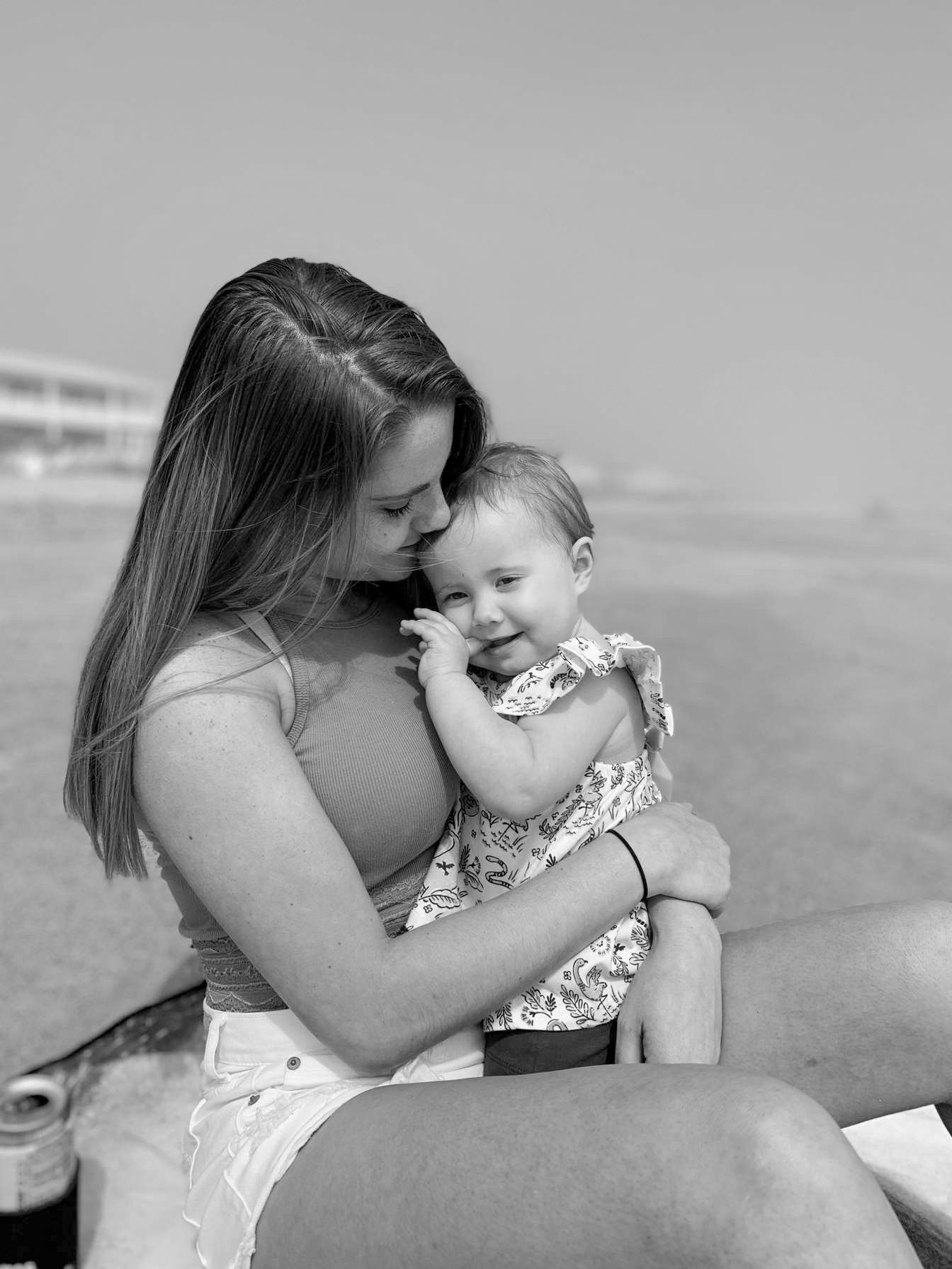 Black and white photo of young woman tenderly holding smiling baby girl on beach.