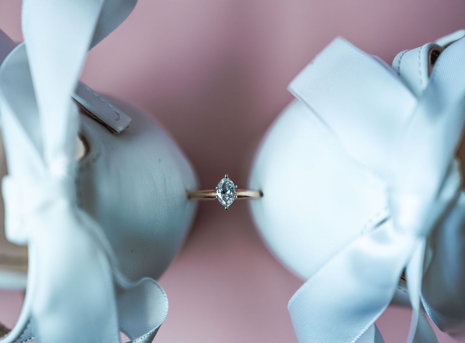 Elegant marquise diamond halo engagement ring displayed between white satin bows on a soft pink background.
