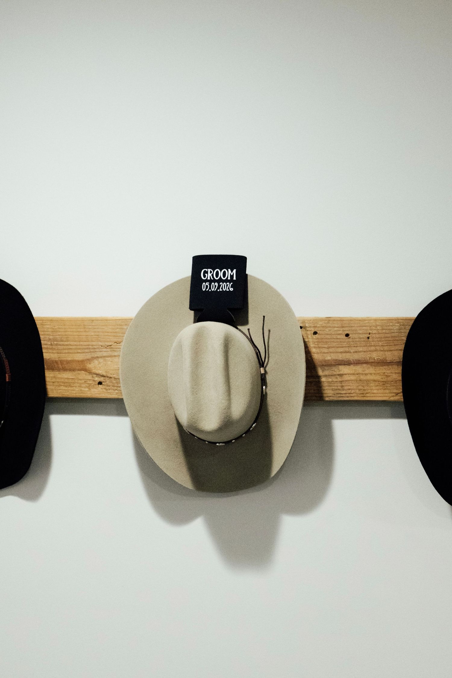 Three cowboy hats displayed on a rustic wooden wall rack, with center hat labeled Groom for a western wedding.