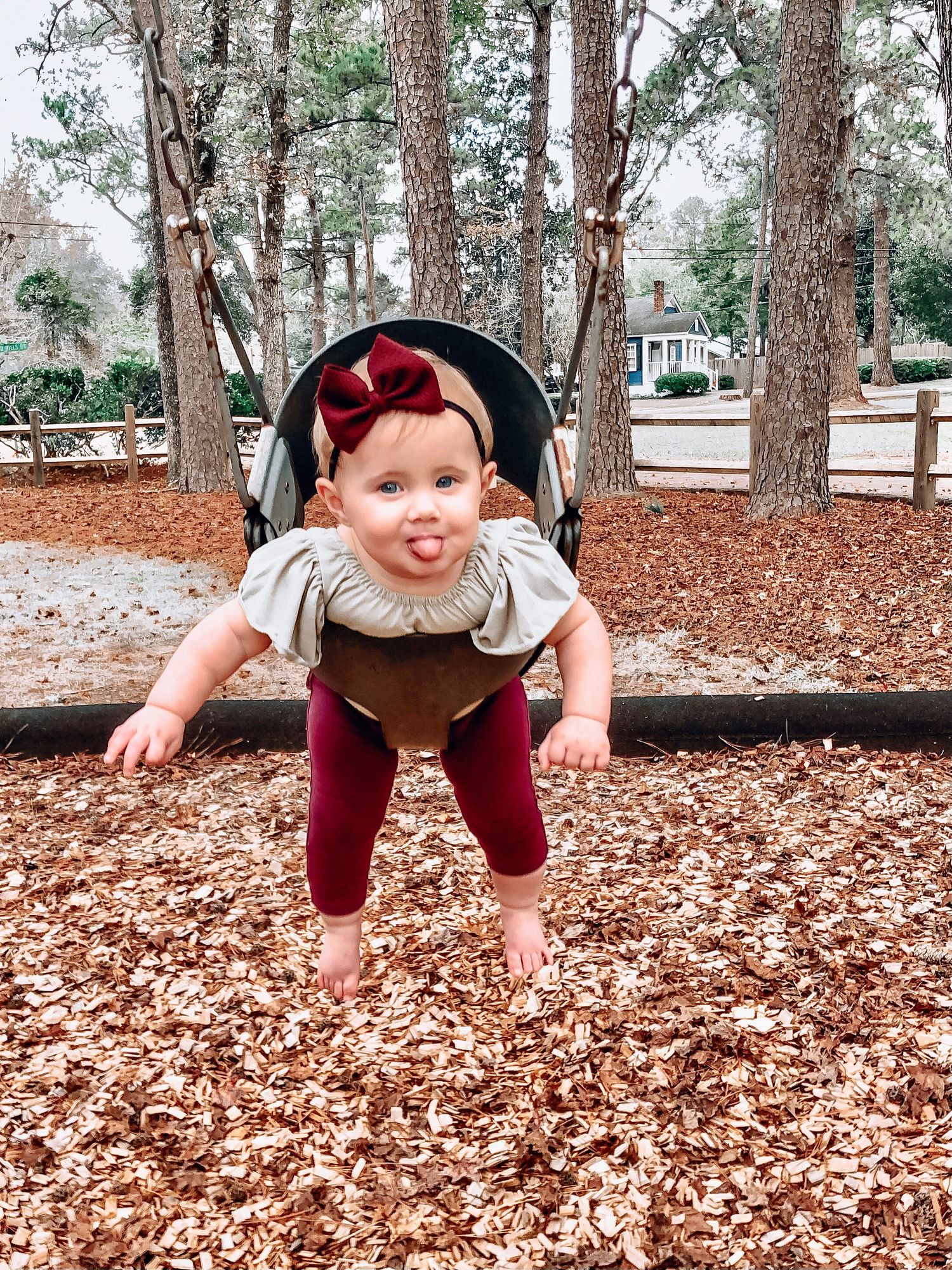 An adorable baby girl with a red bow headband playfully poses on autumn leaves at a park.