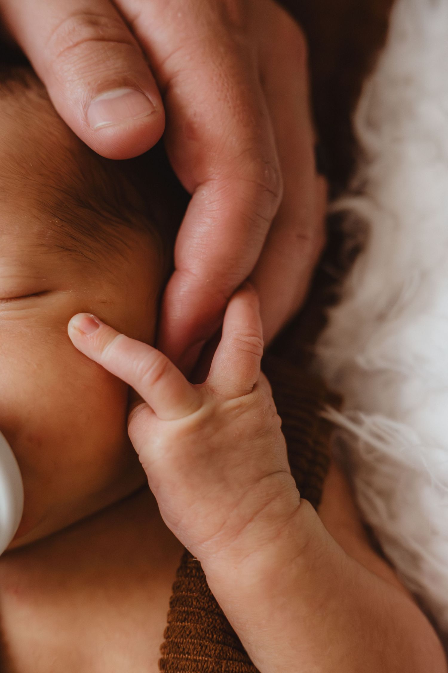 A newborn baby's tiny hand gently gripping an adult's finger, captured in a warm, close-up portrait.