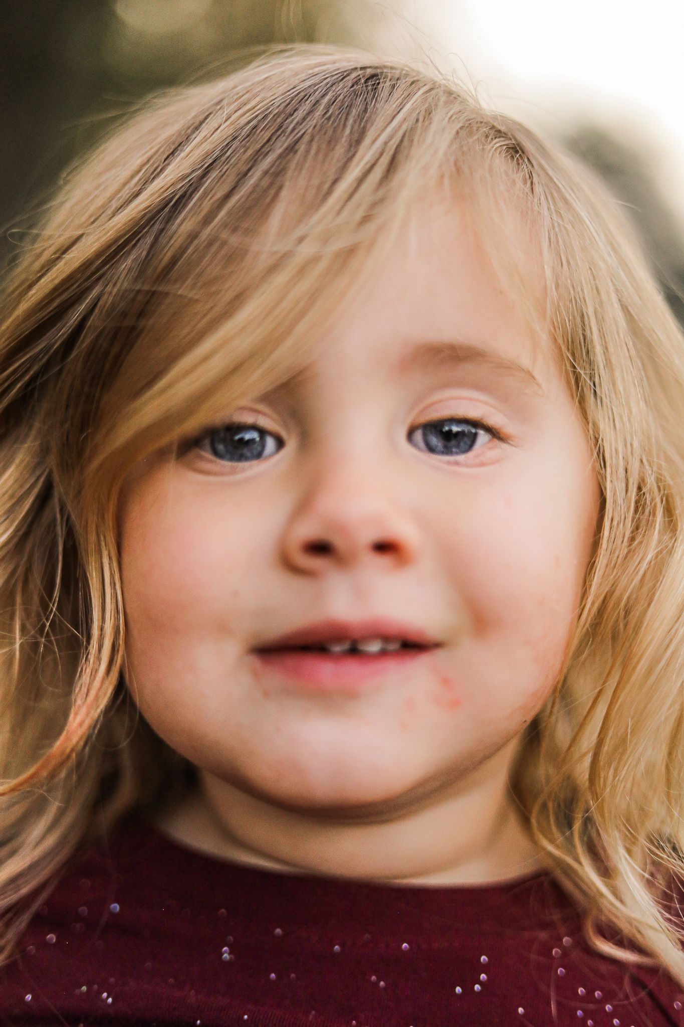 Close-up portrait of a cute blonde toddler girl with blue eyes smiling in warm sunlight.