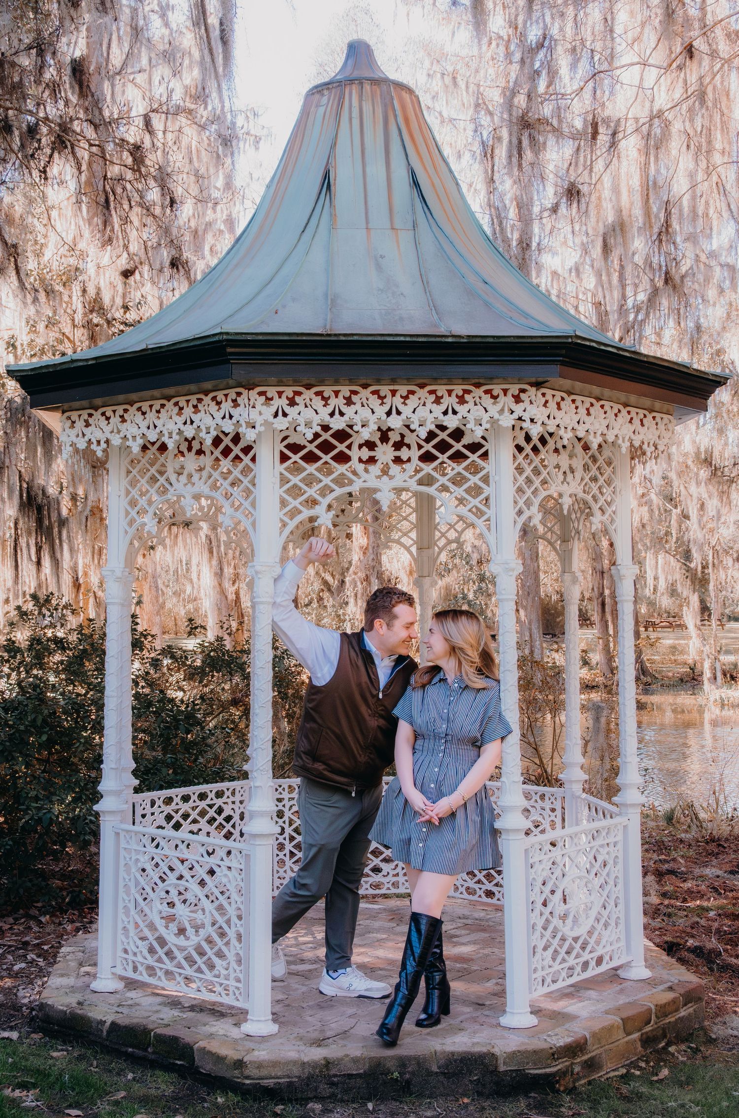 Couple sharing a romantic moment in a white ornate gazebo surrounded by Spanish moss-draped trees near a serene pond.