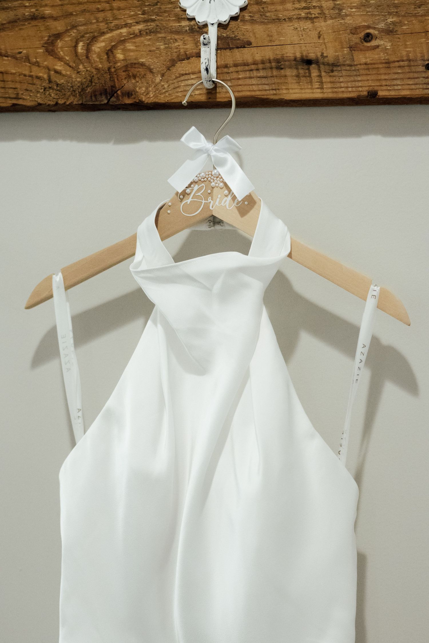 White halter neck wedding dress hanging on a personalized bride hanger against a neutral wall.