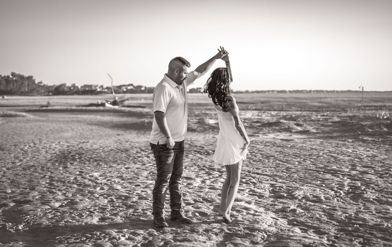 Couple dancing romantically on a sandy beach in black and white photography.