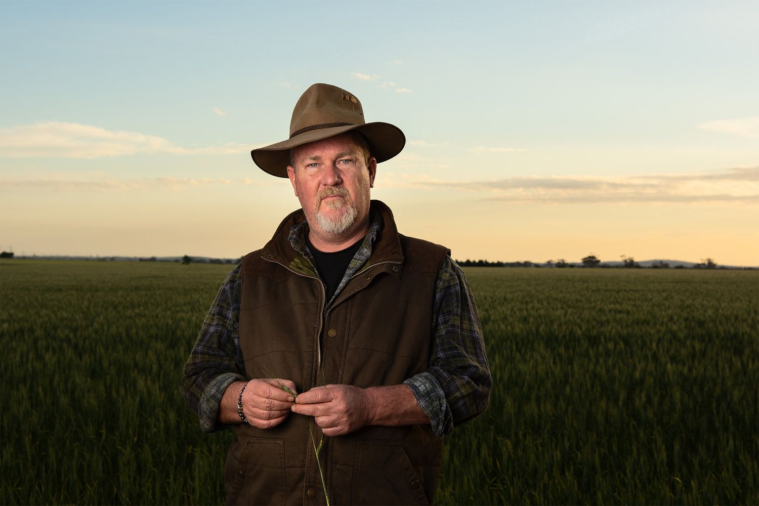 Man wearing a wide brimmed hat standing in the field at sunset.