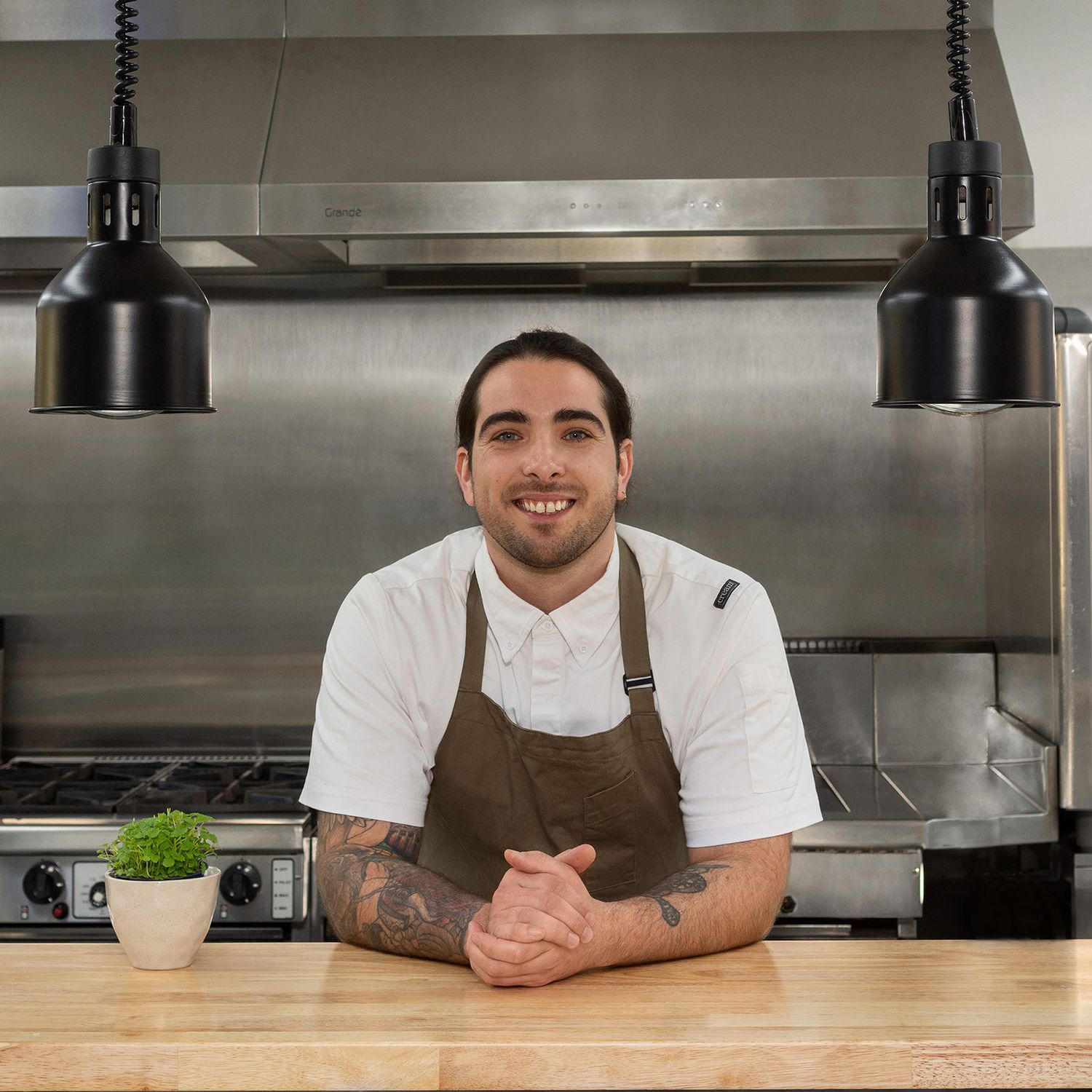 A chef standing in the ktichen leaning on a bench.