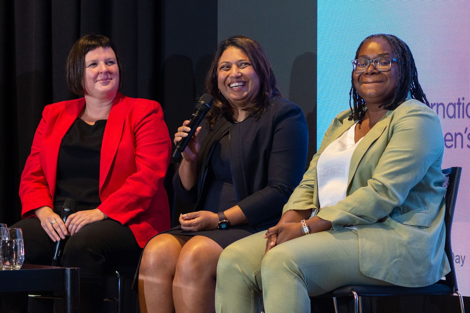 Three female speakers sitting on stage for International Women's Day.