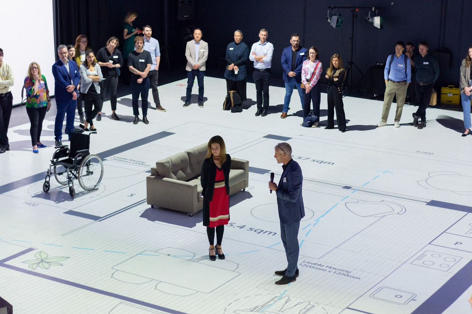A crowd of people looking at an enlarged floor plan projected onto the floor.
