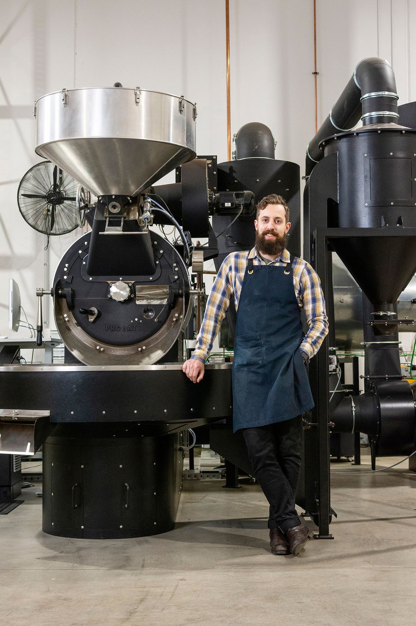 Man standing beside an industrial coffee been roaster.