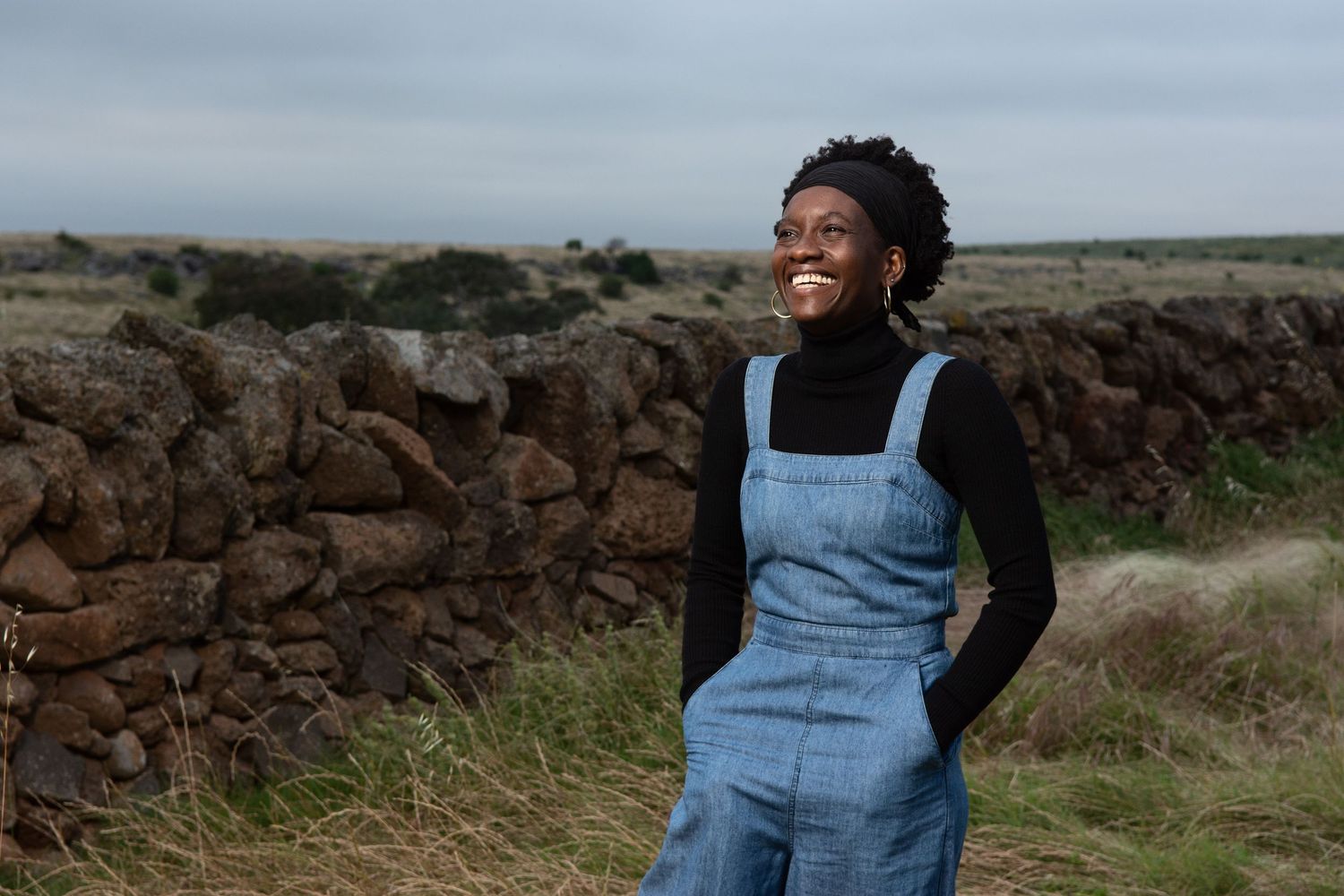Woman dressed in denim overalls standing in a field.