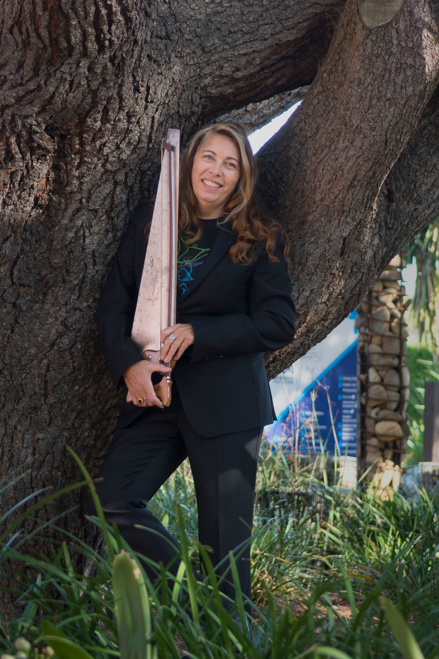 Charlie Barker standing by a tree holding a saw.