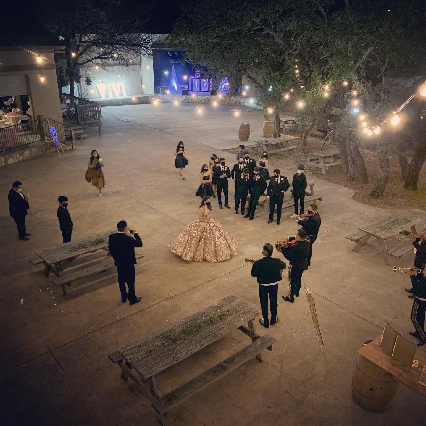 Aerial night view of quinceañera court performing waltz on outdoor patio with string lights at Josabi's Acres in Helotes, Texas