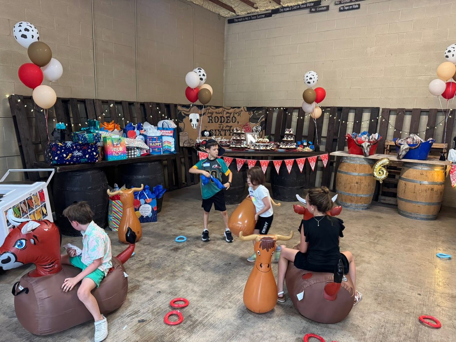 Children playing on animal bouncers at an indoor birthday party with balloon decorations and dessert table at Josabi's Acres in Helotes, TX.