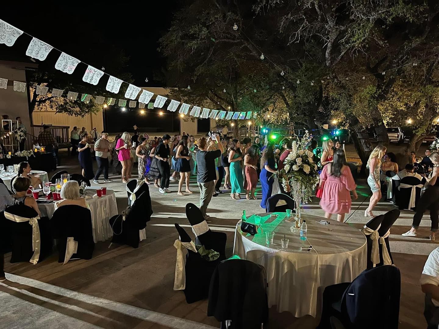 Guests dancing at an outdoor night reception under string lights and papel picado banners at Josabi's Acres in Helotes, Texas.