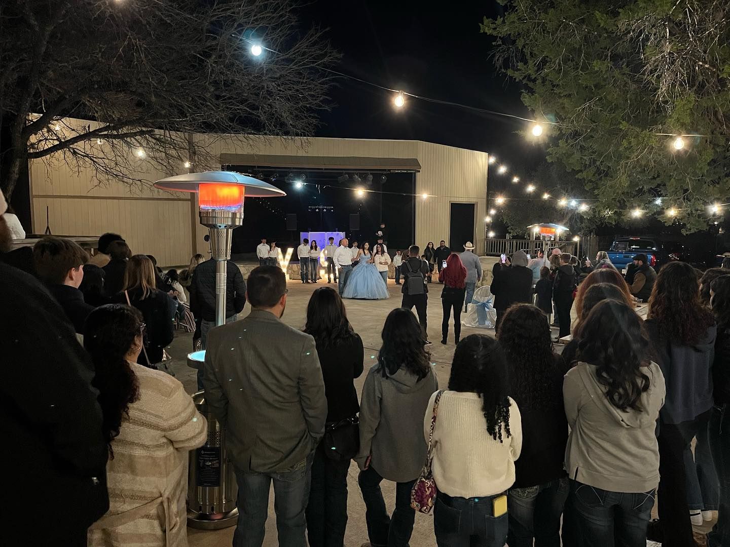 Nighttime outdoor quinceañera celebration with guests gathered around a lit stage with decorations at Josabi's Acres in Helotes TX.