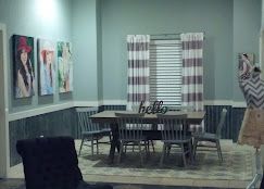 Modern bridal suite with gray wainscoting, striped curtains, wooden table, chairs, and colorful wall art at Josabi's Acres in Helotes, TX.