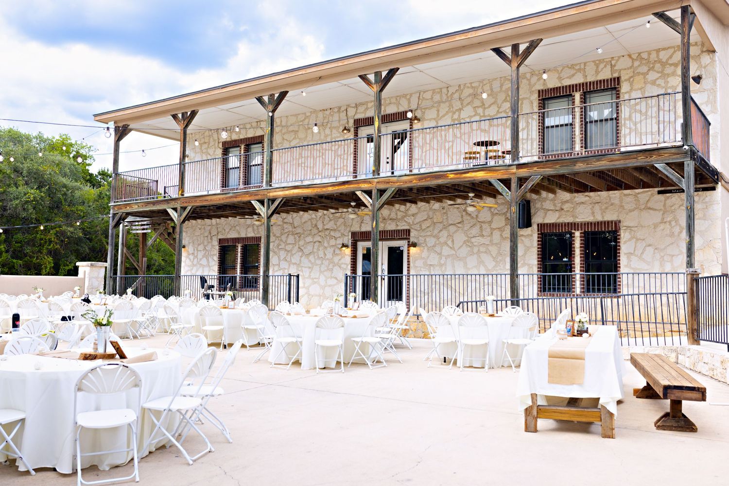 Elegant outdoor wedding reception with white round tables and chairs in front of a two-story stone venue at Josabi's Acres in Helotes, TX.