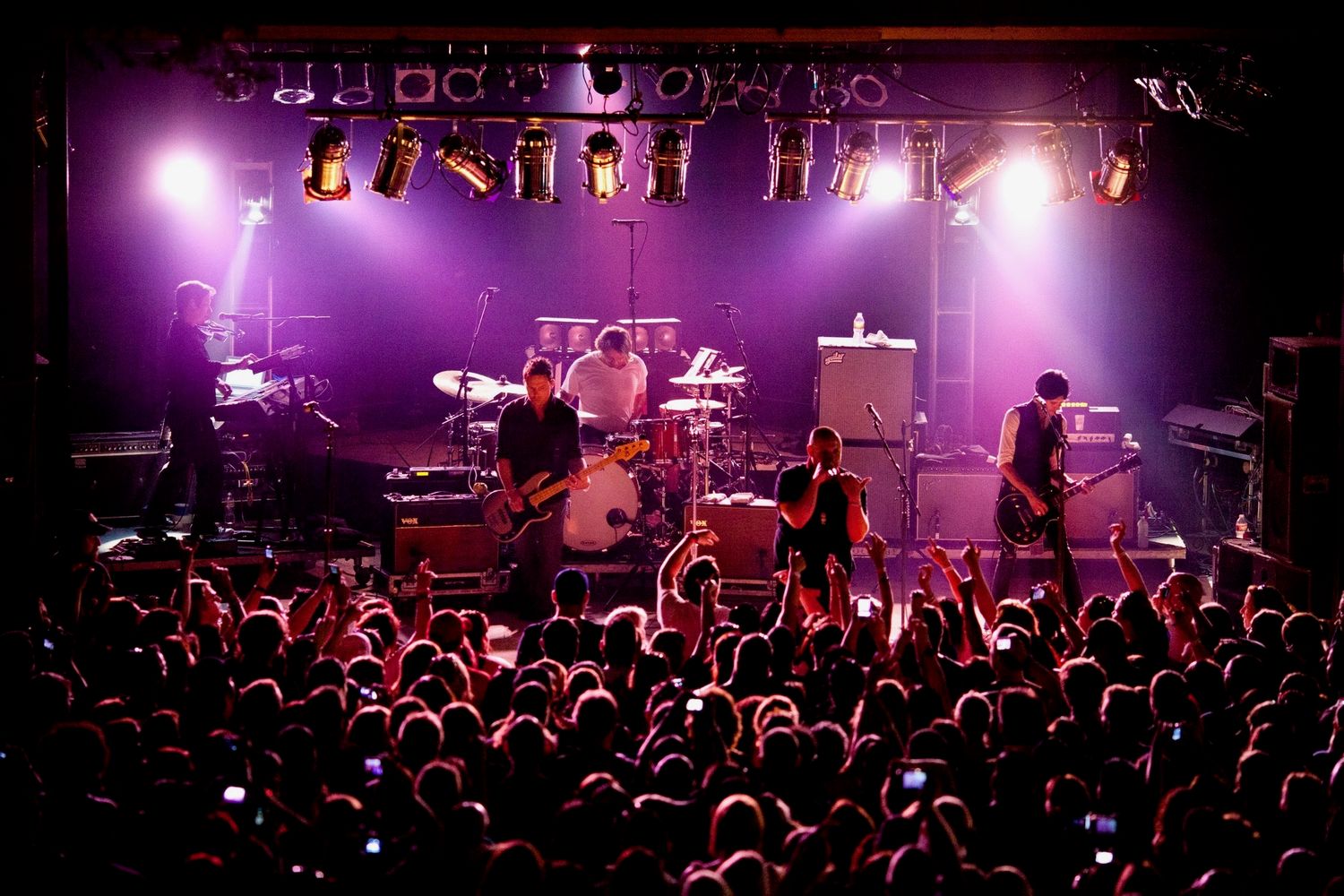 Live rock band performing on a purple-lit stage before a large crowd at Josabi's Live in Helotes, Texas.