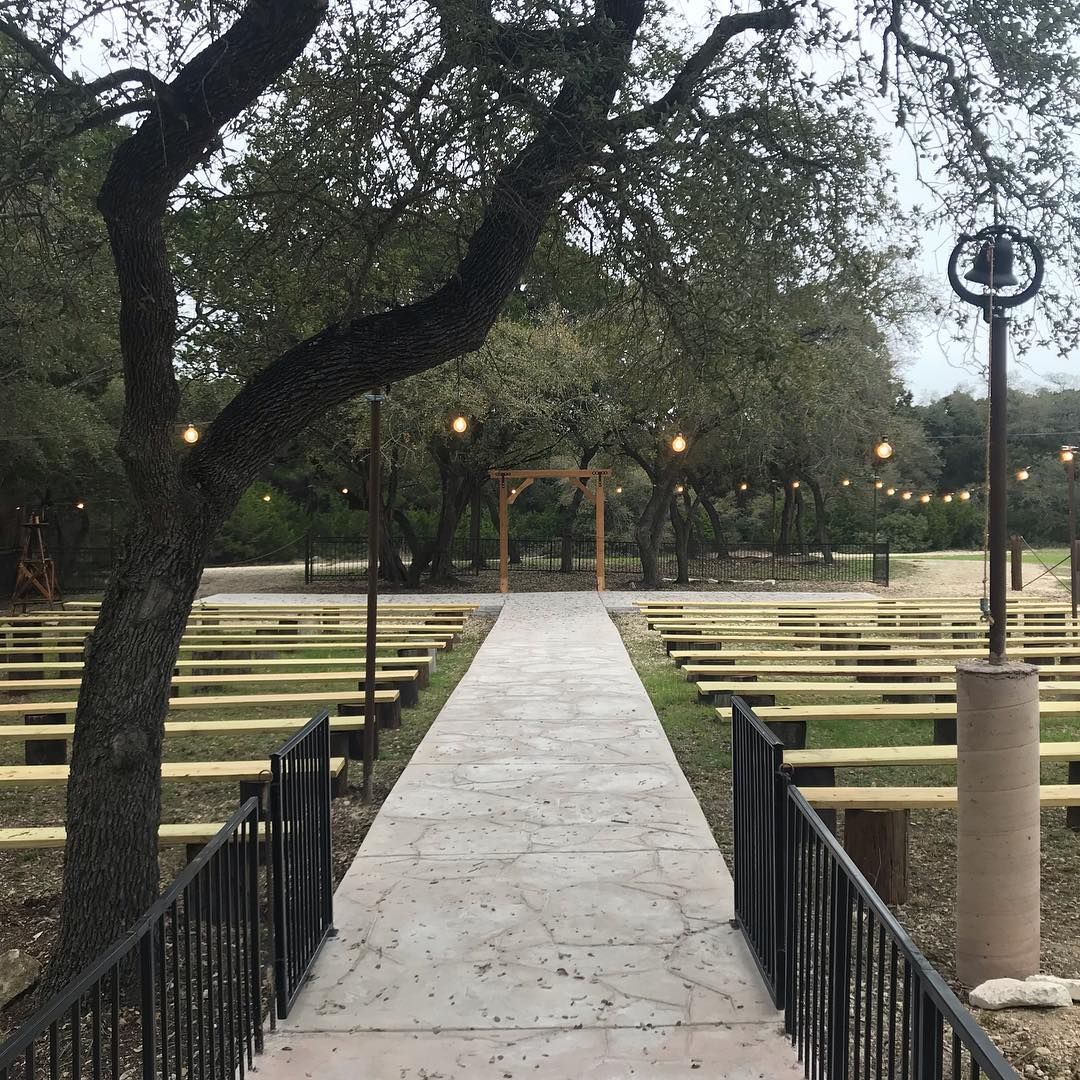 An outdoor wedding ceremony venue with wooden pews, string lights, and an arch at Josabi's Acres in Helotes, Texas